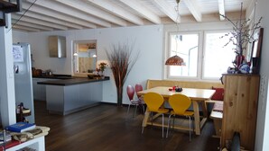 A modern kitchen with a central island, wooden dining table with yellow chairs, and a large window providing natural light.