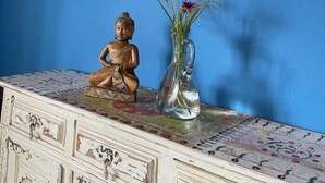 A statue of a seated figure, a vase with flowers, and a patterned table against a blue wall. - Da Silva Surfcamp - Zambujeira Room (Lourinhã)