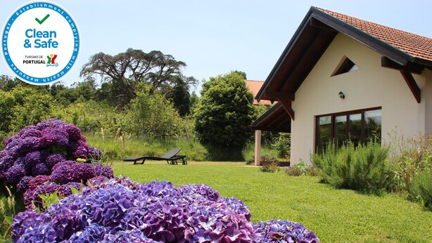 A house with a sloped roof and large windows, surrounded by lush greenery and purple flowers. - Quinta do Pântano is a calm and reserved place, with unique ambience and landscapes (Machico)