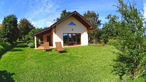 A two-story house with a sloped roof, a covered patio with wooden furniture, and a well-maintained lawn. - Quinta do Pântano is a calm and reserved place, with unique ambience and landscapes (Machico)