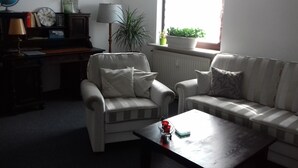 Ein Wohnzimmer mit zwei Sofas, einem Couchtisch, einer Lampe, einem Globus, einer Uhr und einem Fenster mit Pflanzen.