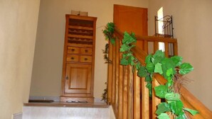 Un escalier en bois, avec une porte en haut, une rampe en bois et du feuillage vert sur le côté droit.
