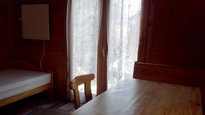 Una habitación pequeña con una mesa de madera, una silla, una cama y una ventana con cortinas de encaje.