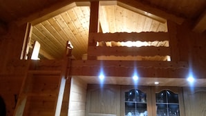Interior de una cabaña de madera con techo inclinado, una ventana de múltiples cristales y una puerta.