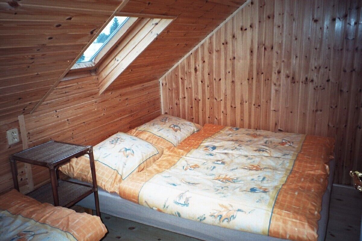 Una pequeña cabaña de madera con techo inclinado, una cama individual con colcha estampada y una pequeña mesa de madera.