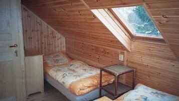 A small attic bedroom with a sloped ceiling, a single bed, a small table, and a window.