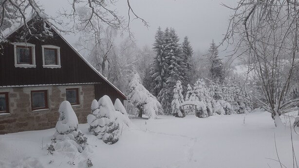A stone house with a dark roof, surrounded by snow-covered trees and a snow-covered lawn. - 4 lovely apartments on beautiful place in mountains in tourist´s and ski area (Bedrichov)