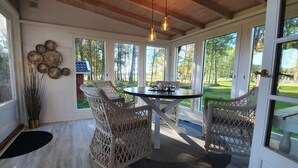 Aurinkoinen huone, jossa on rottinkituoleja, pyöreä pöytä ja suuret ikkunat, joista avautuu näkymä golfkentälle.