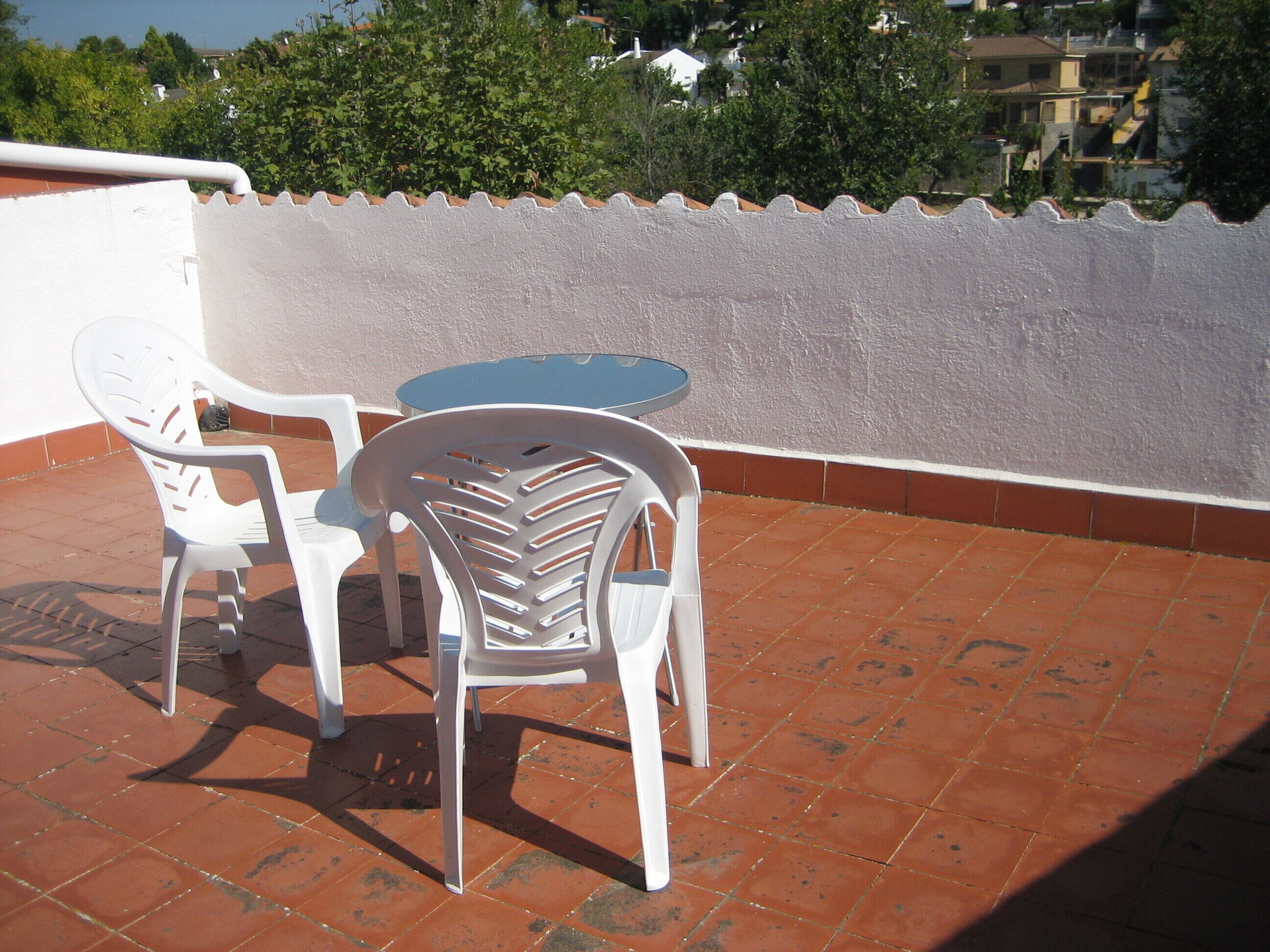 A terrace with a table and two chairs, a white wall, and a tiled floor.