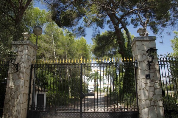 A gated entrance with stone pillars and a metal gate, leading to a building with a white facade and a palm tree in the background. - Duplex apartment with communal pool in Cunit (Can Torrents). (Cunit)
