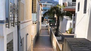 A narrow alleyway with a gated entrance, flanked by buildings with balconies and a mountain in the background. - Apartment/ flat - Playa de Xeraco - XERACO (Xeraco)