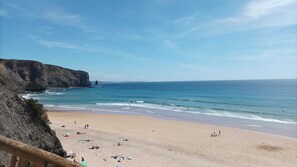 Una playa con barandilla de madera, arena y acantilados rocosos.