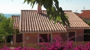 A building with a tiled roof, surrounded by lush greenery and pink flowers.
