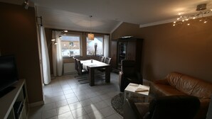 Un salon avec un canapé en cuir marron, une table à manger avec des chaises, un téléviseur et un meuble.