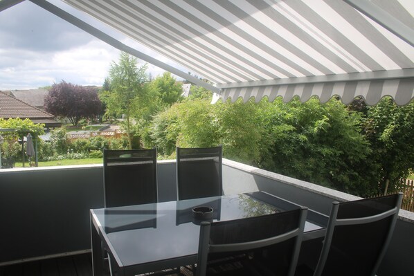 A covered patio area with a glass table and four chairs, surrounded by greenery and a view of the neighborhood. - 4****Fewo, quiet location directly above St Goar, the Rhine and opposite the Loreley (Sankt Goar)