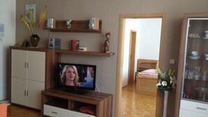 Ett vardagsrum med en TV, träskåp, en bokhylla och en dörr som leder till ett annat rum.