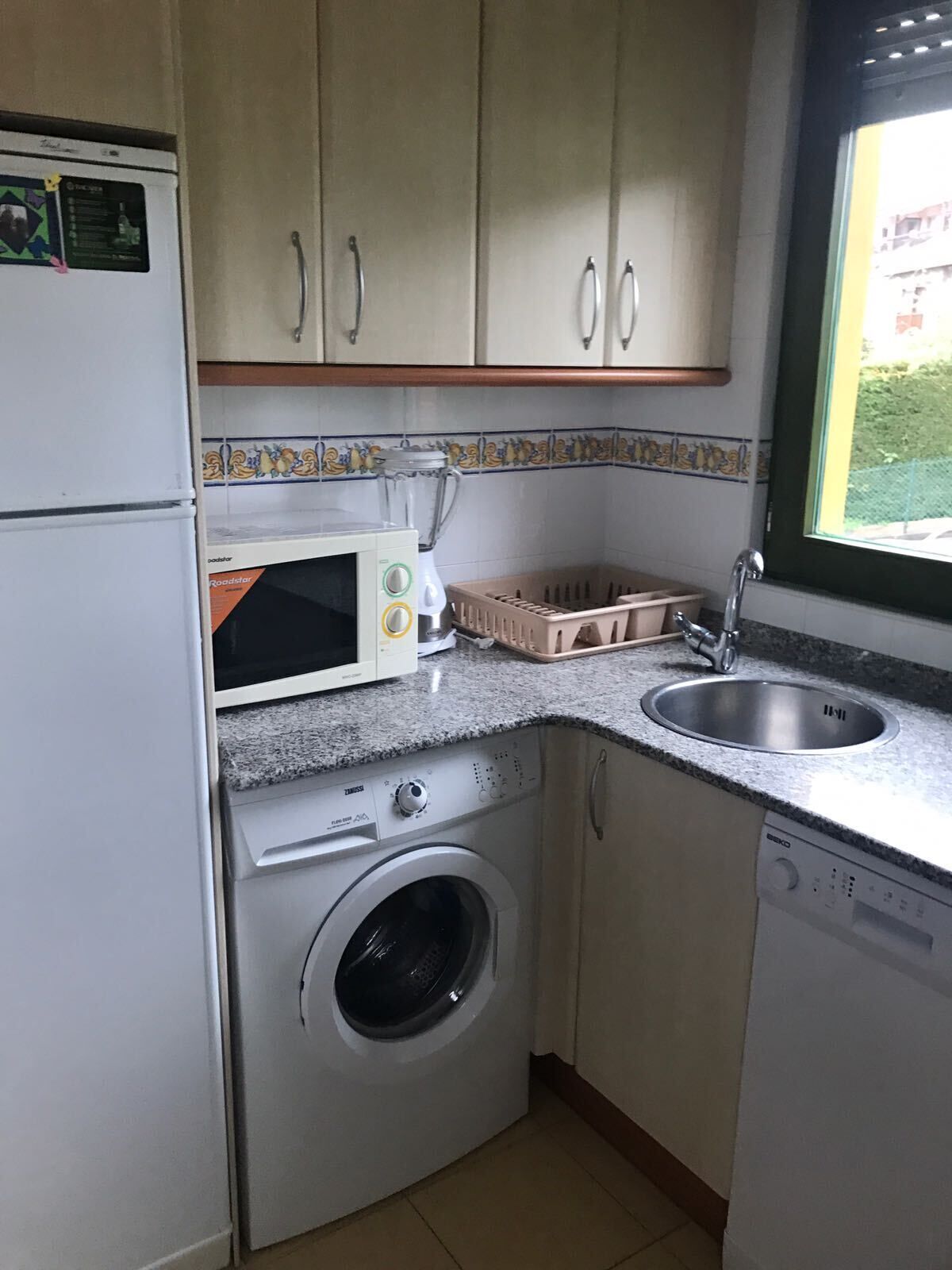A compact kitchen with a washing machine, microwave, and sink.