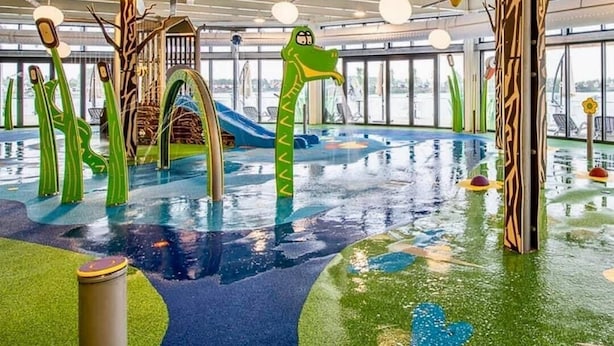 Et indendørs legeområde med pool, rutsjebaner og farverige legetårne.