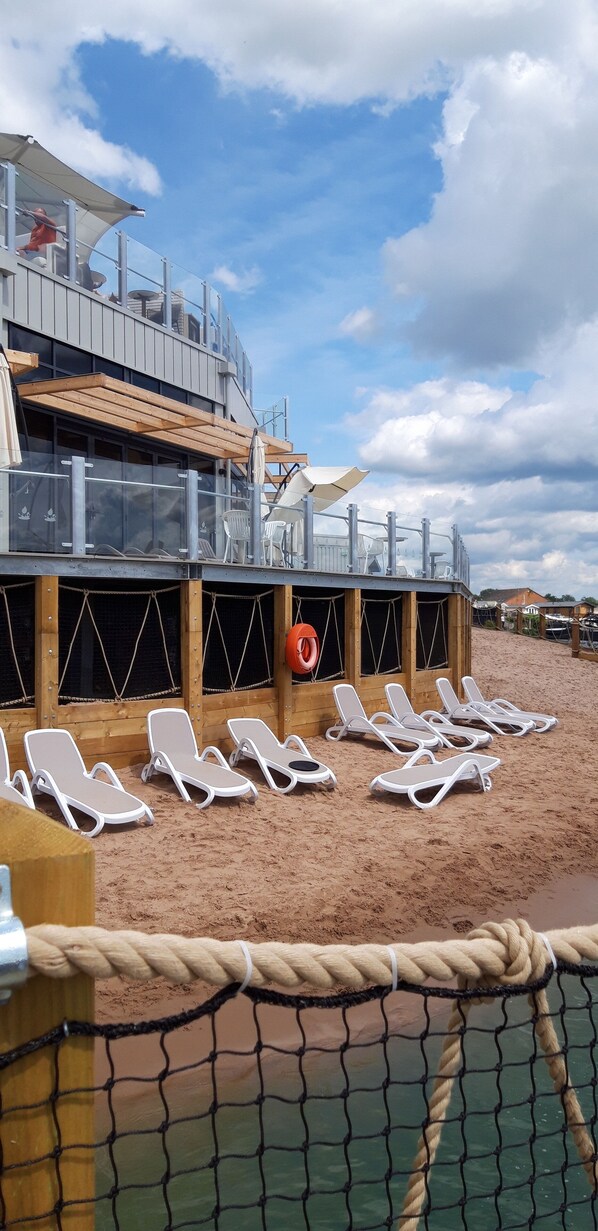 Un bâtiment situé au bord de la plage, doté d’une terrasse en bois et de chaises longues.