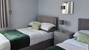 A hotel room with two beds, a bedside table with a lamp, a wall-mounted mirror, and a ceiling light fixture.