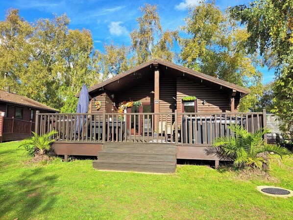 Une cabane en bois dotée d’un porche, entourée d’herbe et d’arbres.