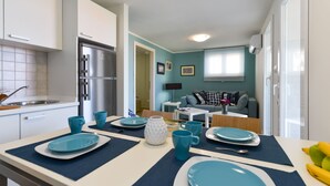 A compact kitchen with a refrigerator, sink, and dining area with blue plates and cups. - Apartment Mare with beautiful sea views (Lun)