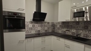 A modern kitchen with white cabinets, a black countertop, a built-in oven, a microwave, and a patterned backsplash.