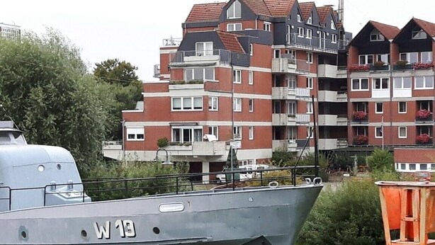 A boat with the number W 13 docked near a residential area with multi-story buildings.