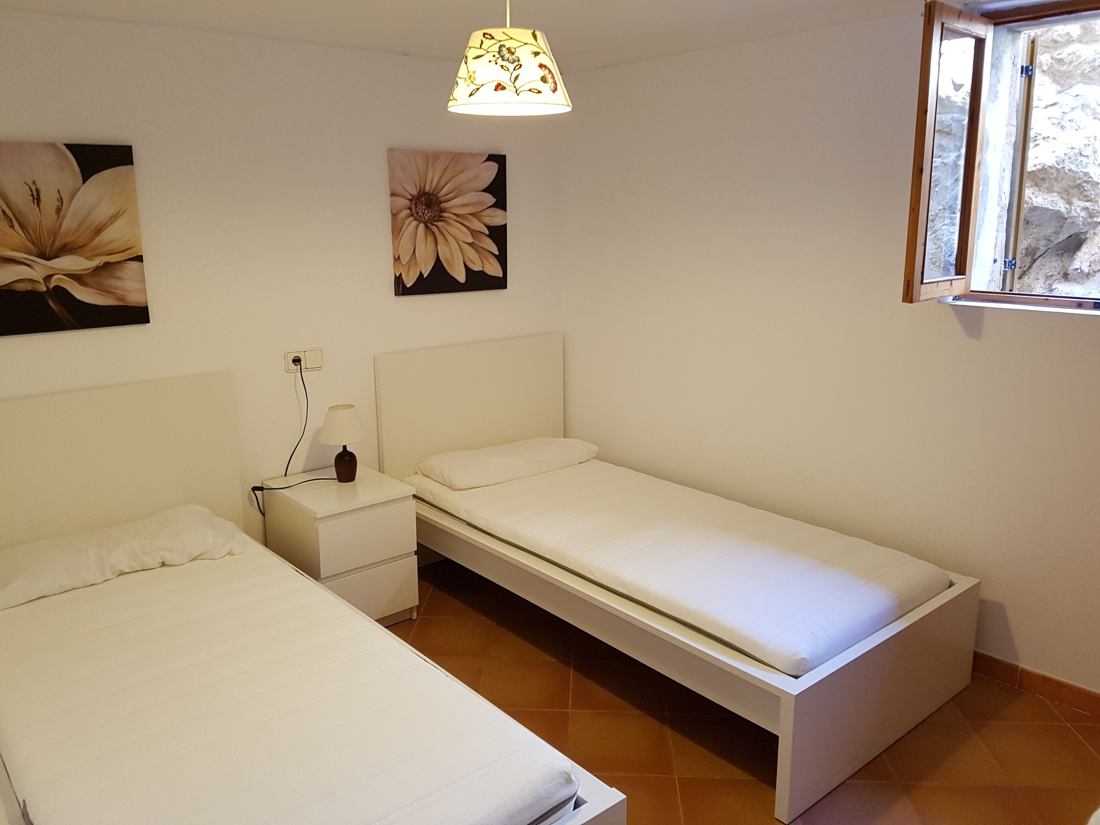 Un dormitorio con dos camas, una mesita de noche, una lámpara y una ventana.