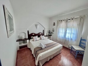 Una camera da letto con un letto, comodini, una sedia, una finestra con tende e una mensola a muro.