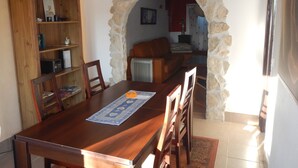 Un comedor con una mesa y sillas de madera, una estantería y un arco de piedra que da a una sala de estar.