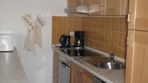 Een compacte keuken met houten kastjes, een inbouwvaatwasser en een koffiezetapparaat.