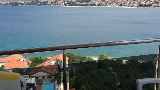 Een balkon met uitzicht op een kustplaats, een zwembad en een bergketen op de achtergrond.