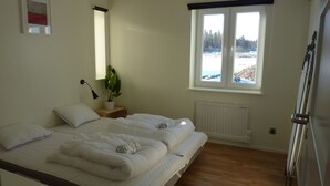 Makuuhuoneessa on kaksi sänkyä, ruukkukasvi, ikkuna, josta avautuu näkymä lumiseen maisemaan, ja patteri.