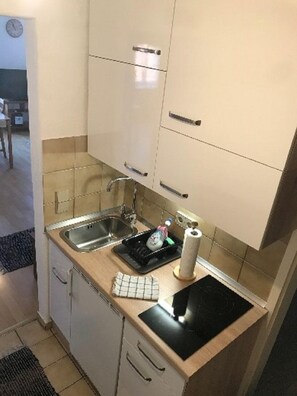 Une cuisine de taille réduite, dotée de deux éviers, d’un plan de travail noir et d’une cuisinière.