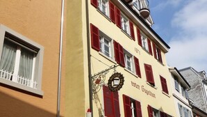 A multi-story building with a yellow facade, red shutters, and a sign reading "Roter Gugelmann." - Over the rooftops of the historic old town, center in the pedestrian zone (Konstanz)