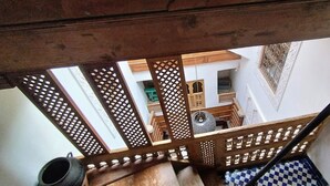 Een houten trap met ingewikkelde spijlenwerkdecoraties, die leidt naar een kamer met een patroon in de vloer en een zichtbare deur.