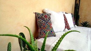 Een bed met gebogen kussens en een witte spreidek, omringd door cactussen en een kamerplant.