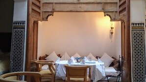 A dining area with a table set for two, surrounded by wooden chairs, under a wooden archway.