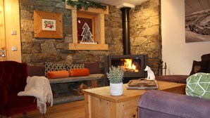A cozy living room with a stone wall, a wooden bench, a red velvet chair, and a fireplace.