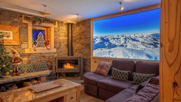 A cozy living room with a stone fireplace, a large window with a snowy mountain view, a plush brown sofa, and a Christmas tree.