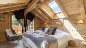 A cozy wooden cabin room with a large bed, a chair, and a skylight.