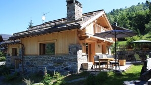 A stone and wood cabin with a patio area, outdoor seating, and a chimney.