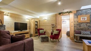 A cozy living room with wooden walls, a stone accent wall, a television, and two red armchairs.