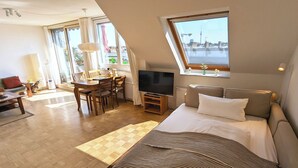 A modern hotel room with a large bed, a TV, a dining area with a table and chairs, and a view of a cityscape through the window. - Over the roofs of Berlin with lift and a great view at the TV tower (Berlin)