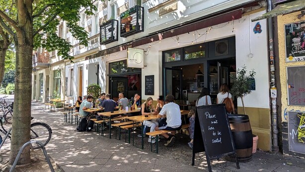 An outdoor café with wooden tables and benches, a chalkboard menu, and a sign requesting patrons to seat themselves. - Over the roofs of Berlin with lift and a great view at the TV tower (Berlin)