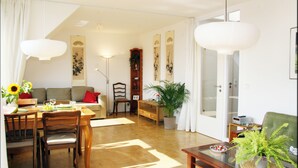 A spacious living room with a dining area, a sofa, a bookshelf, and a large potted plant. - Over the roofs of Berlin with lift and a great view at the TV tower (Berlin)