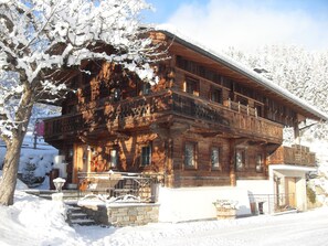 A wooden chalet with a balcony, surrounded by snow-covered trees.