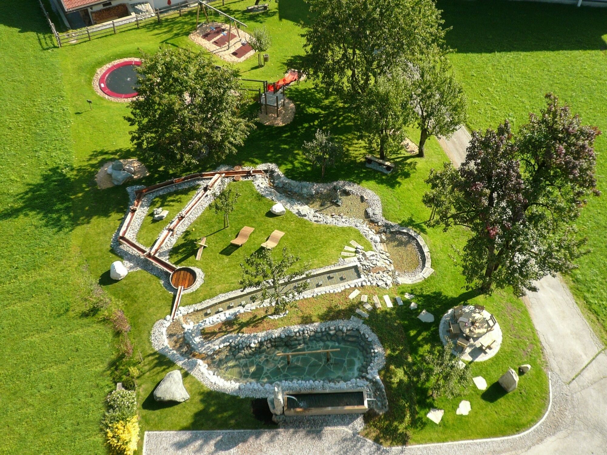 Vista aérea de un parque con una estructura de piedra circular, zonas de descanso y un pequeño estanque.