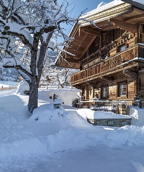 A wooden chalet with a balcony, surrounded by snow-covered trees and a clear sky.